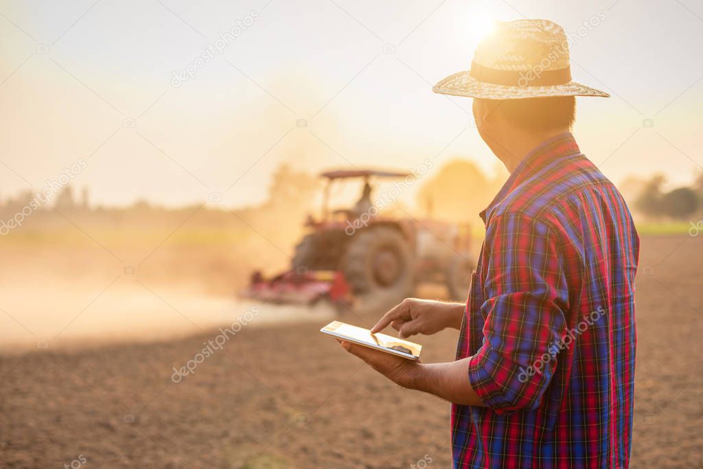 Asian young farmer working and holding tablet in the empty land.