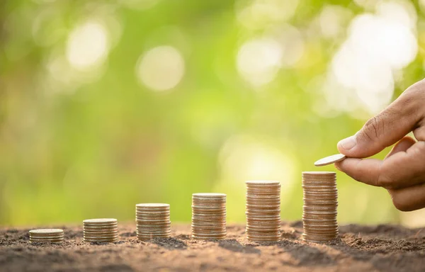 Hand putting coins in stack on wooden plank with green blur back — Stock Photo, Image