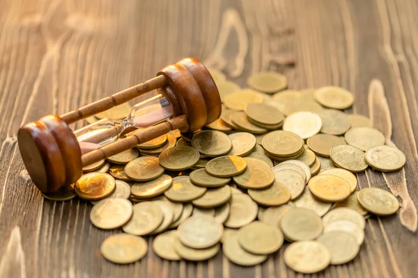 Vintage hourglass or sandglass and coin on wooden table. Saving — Stock Photo, Image