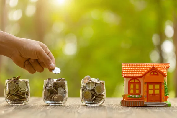 Hand zet de munt aan spaarvarken bank (Home Model) op groene natuur blu — Stockfoto