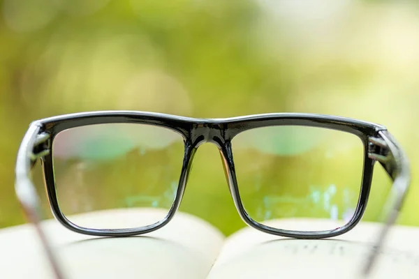 Book and eye glasses on wooden table with abstract green nature — Stock Photo, Image