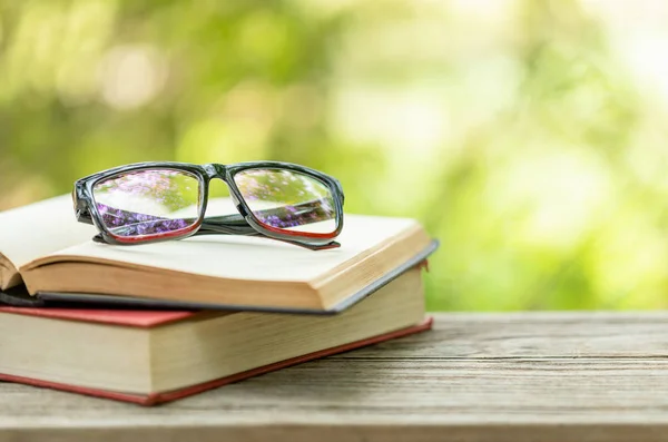Γυαλιά βιβλίων και ματιών σε ξύλινο τραπέζι με αφηρημένη πράσινη φύση — Φωτογραφία Αρχείου
