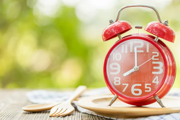 Red alarm clock, Fork, and spoon on wooden table with green outd