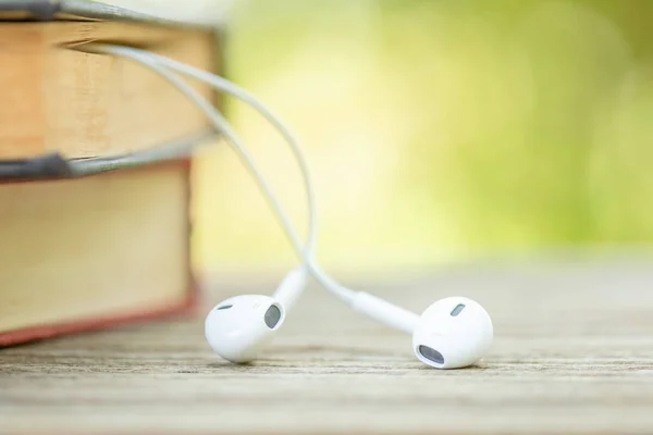 Book and white earphone on wooden table with abstract green natu — Stock Photo, Image