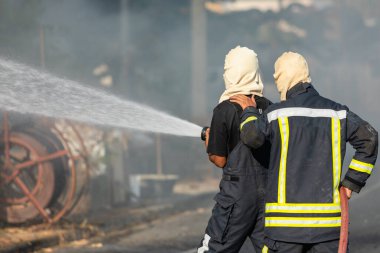 İtfaiyeci ya da itfaiyeci yangın çıkmasın diye büyük su hortumundan su püskürtüyor.