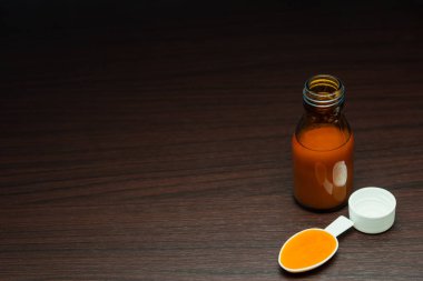İlaç şişesinde şurup ilacı ve koyu kahverengi tahta bir masada ilaç kaşığı.. 