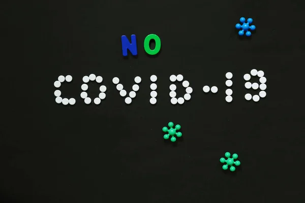Siyah arka planda beyaz hapların tıbbi maskesiyle yazdığı Covid-19 yazısı.