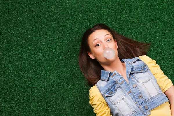 Woman blowing bubble gum while lying on the grass — Stock Photo, Image