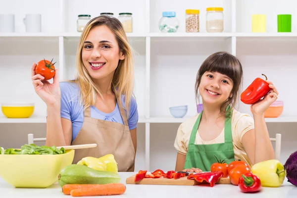 Madre e hija mostrando tomate y pimienta mientras hacen comida saludable —  Fotos de Stock