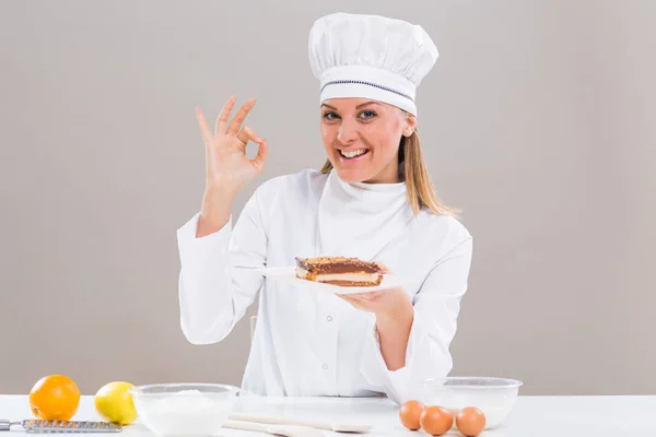 Vrouwelijke banketbakker met plakje cake weergegeven: ok teken — Stockfoto