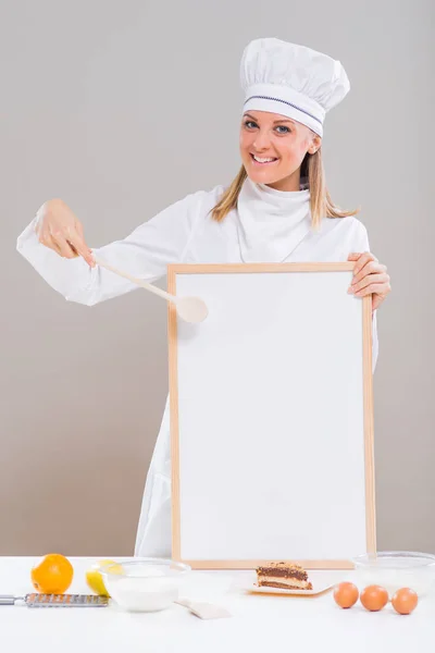 Vrouwelijke banketbakker met whiteboard, plakje cake en ingrediënten — Stockfoto