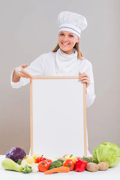 Női szakács faliújság és zöldségekkel — Stock Fotó