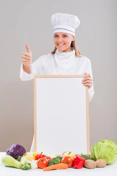 Шеф-повар с белой доской и овощами, показывающими большой палец вверх — стоковое фото