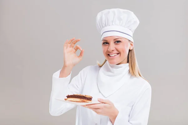 Vrouwelijke banketbakker met plakje cake gebaren — Stockfoto