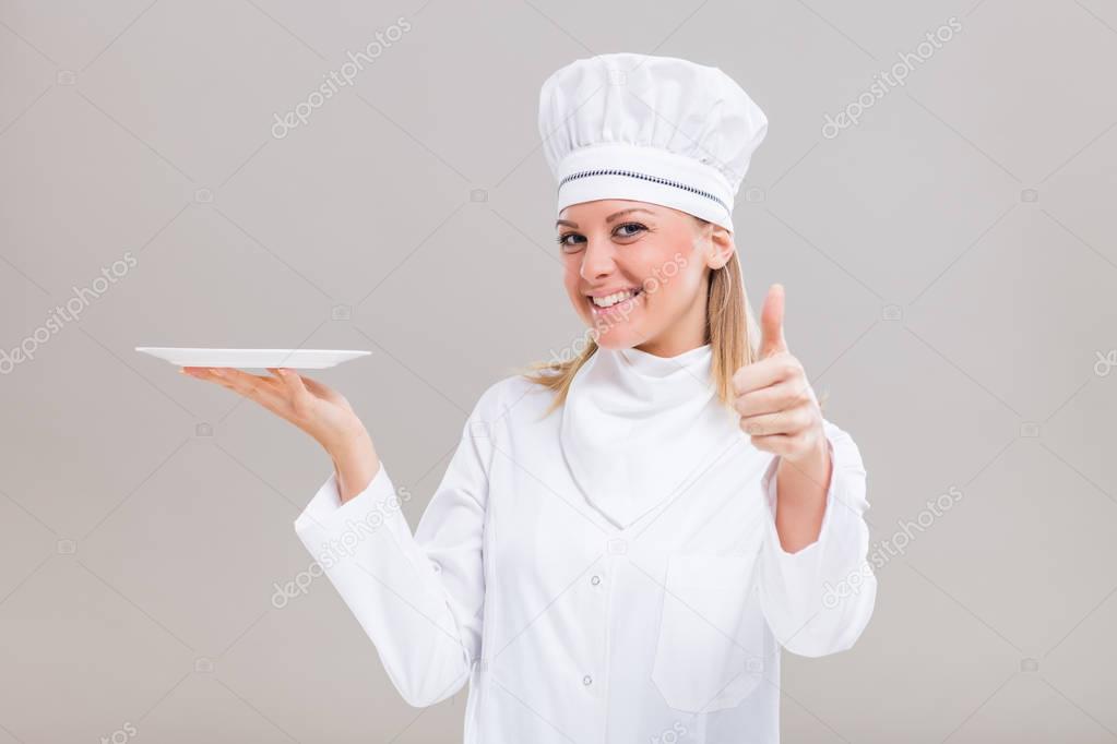Female chef holding plate and showing thumb up