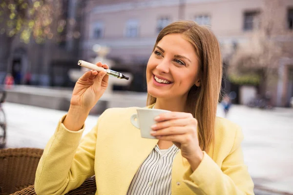 Woman using electronic cigarette and drinking coffee