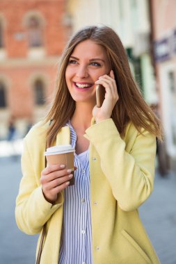 Kadın cep telefonu kullanıyor ve kahve içiyor. 