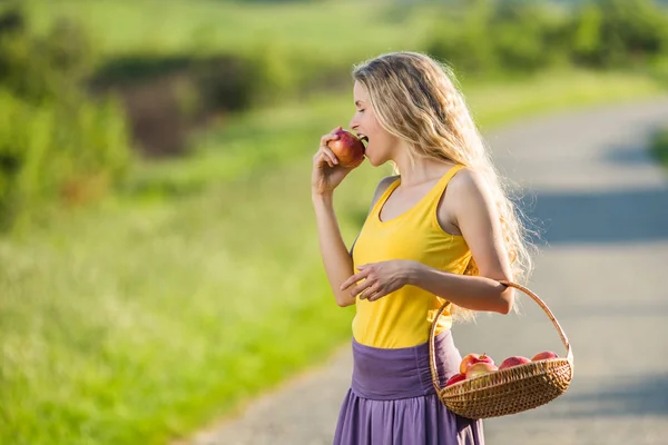 Όμορφη γυναίκα που στέκεται στο δρόμο της χώρας και διατροφικές apple. — Φωτογραφία Αρχείου