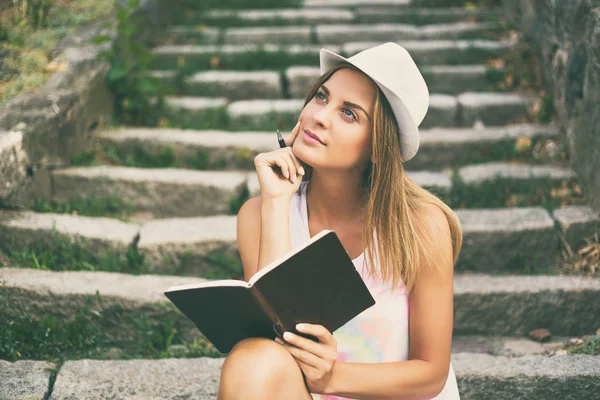 Junge Frau denkt und schreibt in ihr Notizbuch — Stockfoto