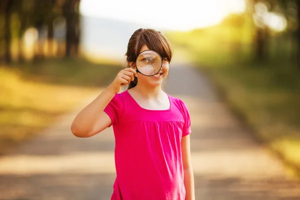 Söt liten flicka med förstoringsglas i naturen — Stockfoto