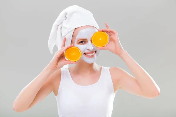 Женщина в маске для лица держит кусочки апельсина — стоковое фото