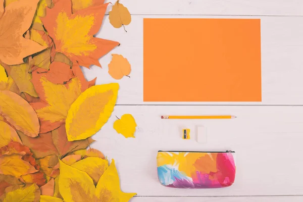 Papier orange et fournitures scolaires sur table en bois avec feuilles peintes — Photo