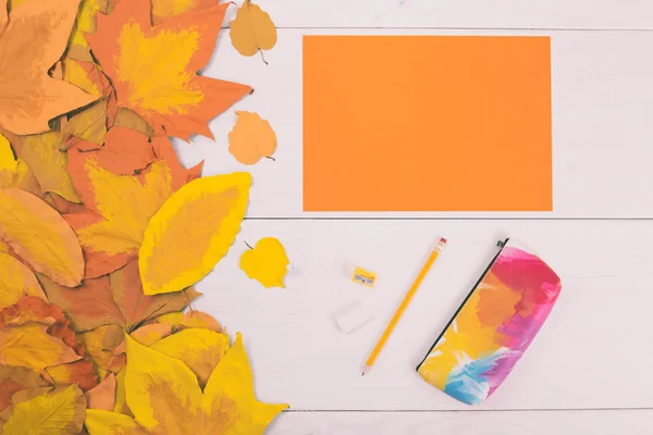 Papier orange et fournitures scolaires sur table en bois avec feuilles peintes — Photo