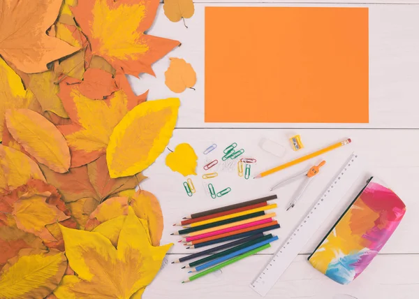 Papier orange et fournitures scolaires sur table en bois avec feuilles peintes — Photo