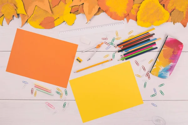 Farbige Papiere und Schulbedarf auf Holztisch mit bemalten Blättern — Stockfoto