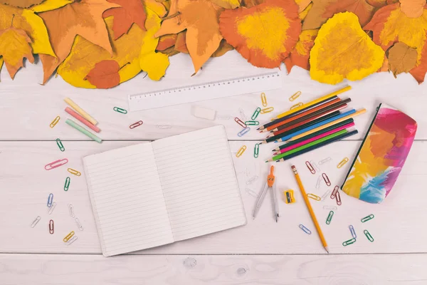Notizbuch und Schulbedarf auf Holztisch mit bemalten Blättern — Stockfoto