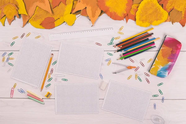 Leere Papiere und Schulbedarf auf Holztisch mit bemalten Blättern — Stockfoto