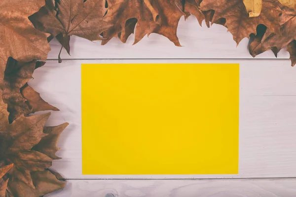 Порожній жовтий папір на дерев'яному столі з осіннім листям — стокове фото
