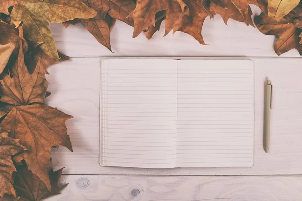 Блокнот і ручка на дерев'яному столі з осіннім листям — стокове фото
