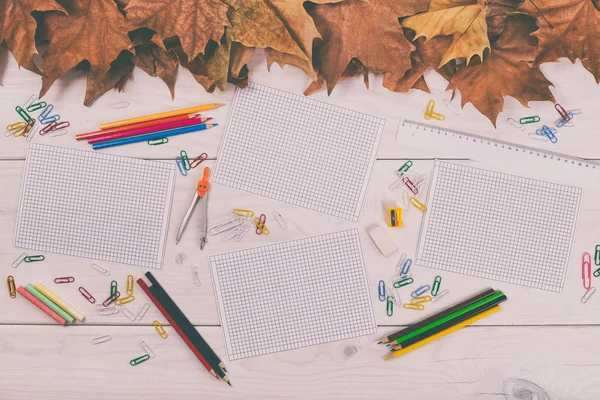 Папери та шкільне приладдя на дерев'яному столі з осіннім листям — стокове фото