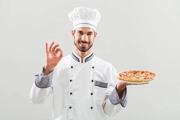 Szef kuchni gospodarstwa pizza i pokazuje znak ok — Zdjęcie stockowe