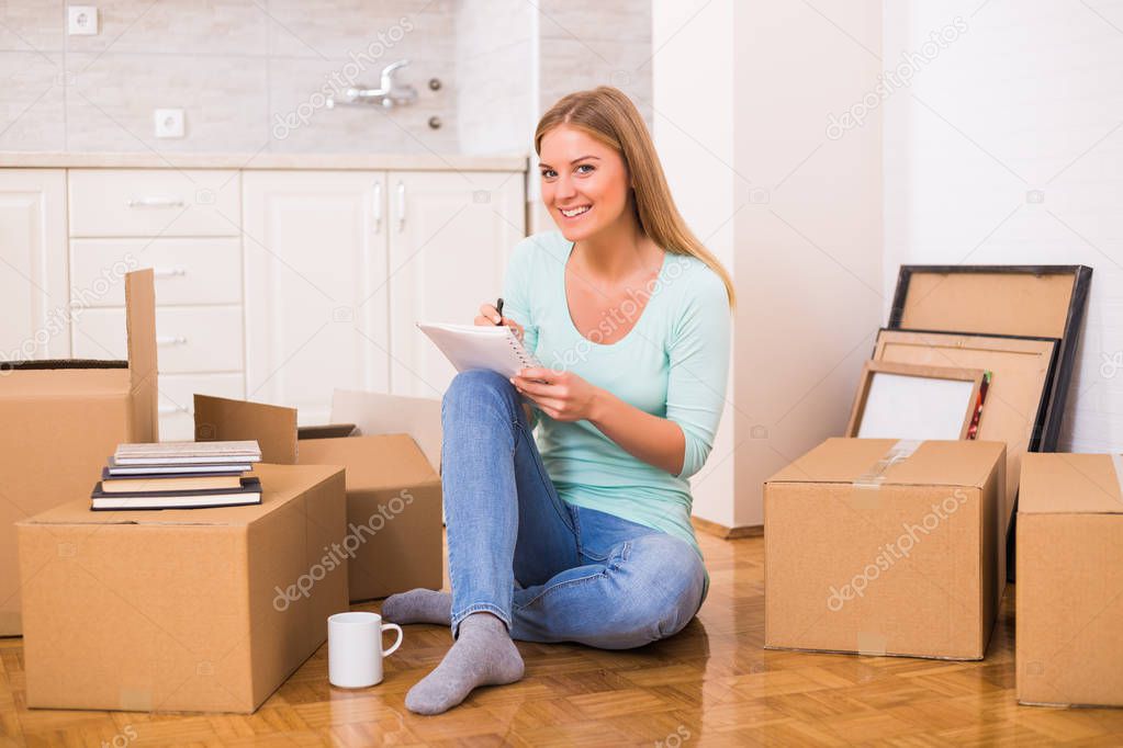 Beautiful woman writing in notebook while moving in new home.