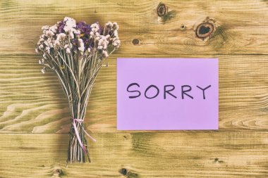 Bir buket çiçek ile haber tahta masada özür. Görüntü kasten tonda.