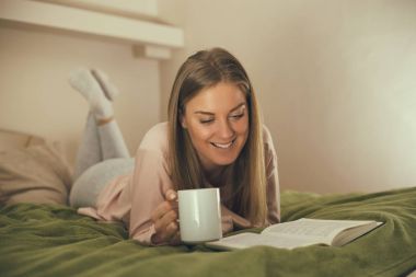 Güzel kadın bir kitap okuma ve kahve içme sahiptir. Görüntü kasten tonda.