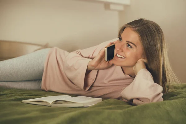 Hermosa Mujer Que Usa Teléfono Mientras Lee Libro Descansa Dormitorio — Foto de Stock