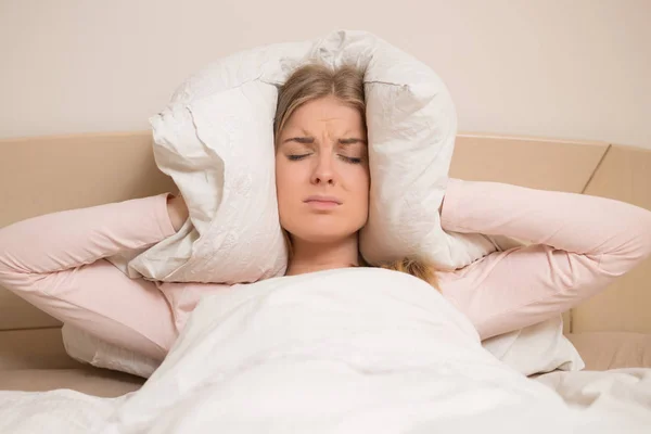 愤怒的女人 试图睡觉和覆盖她的耳朵与枕头干扰 — 图库照片