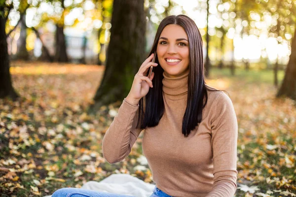 美丽的女人坐在公园里 一边打电话一边享受秋天的快乐 — 图库照片