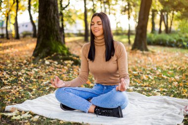 Güzel bir kadın dinlenirken meditasyon yapıyor ve sonbaharda parkta eğleniyor..