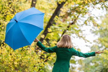 Woman  with her arms outstretched holding umbrella while standing in the park.