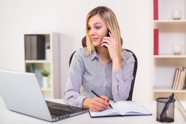 İş kadını ofisinde çalışırken cep telefonu kullanıyor..