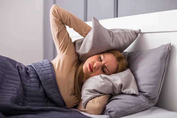 愤怒的女人 试图睡觉和覆盖她的耳朵与枕头干扰 — 图库照片