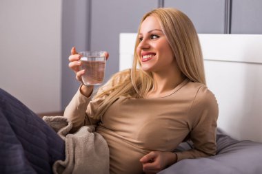 Beautiful woman drinking water and sitting on bed.