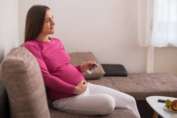妊娠中の女性はソファに座って超音波画像を保持 — ストック写真