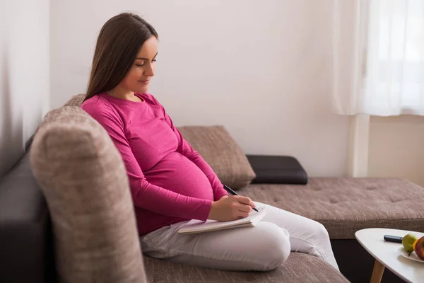 Glückliche Schwangere Frau Schreibt Ihr Notizbuch Während Sie Zeit Hause — Stockfoto