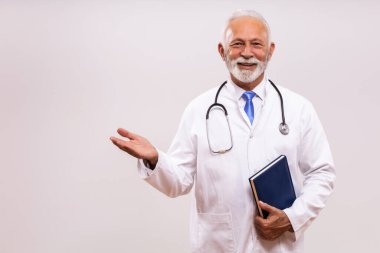 Kıdemli doktorun portresi kişisel düzenleyiciyi tutuyor ve gri arka planda hoş bir jest yapıyor..