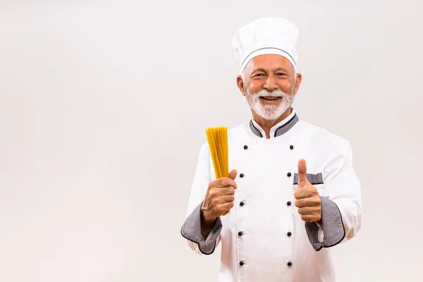 高级厨师拿着意大利面 在灰蒙蒙的背景上露出大拇指的画像 — 图库照片